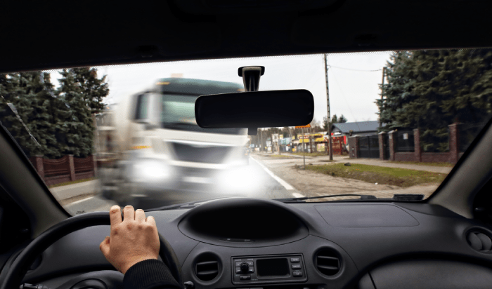 A person driving a car with a truck following closely behind on a road.