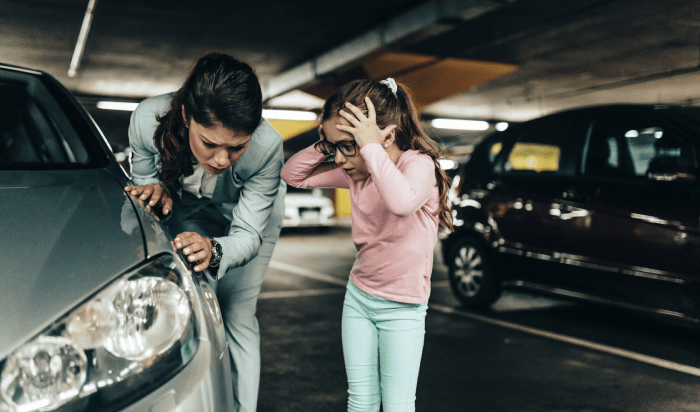 A woman and a little girl examining a car, possibly discussing its damages.