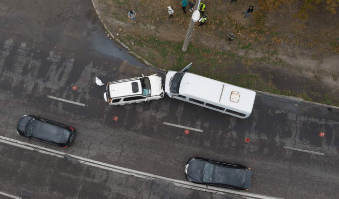 An aerial view of a car and a bus collide on a road.