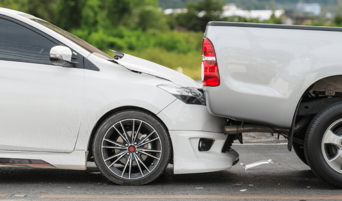 A white car being struck by a truck on a road.